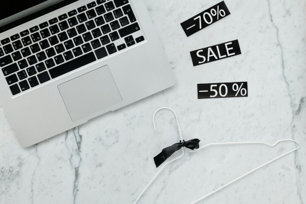Flat lay of a laptop, hanger, and sale stickers on a marble desk, ideal for Black Friday themes.